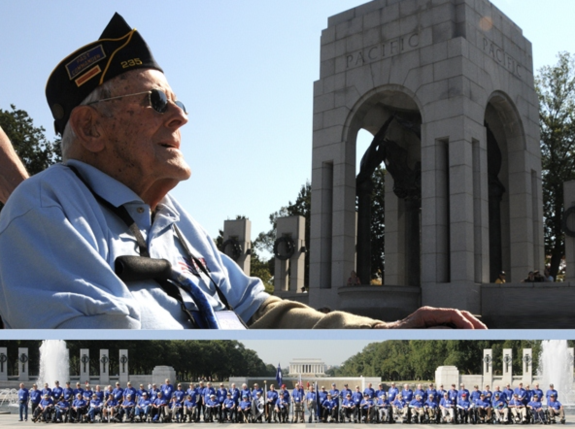 A WWII Pacific Theater veteran in garrison cap and sunglasses looking toward the pillars of the National WWII Memorial, with a long row of fellow veterans in blue shirts seated and standing in formation beneath him.